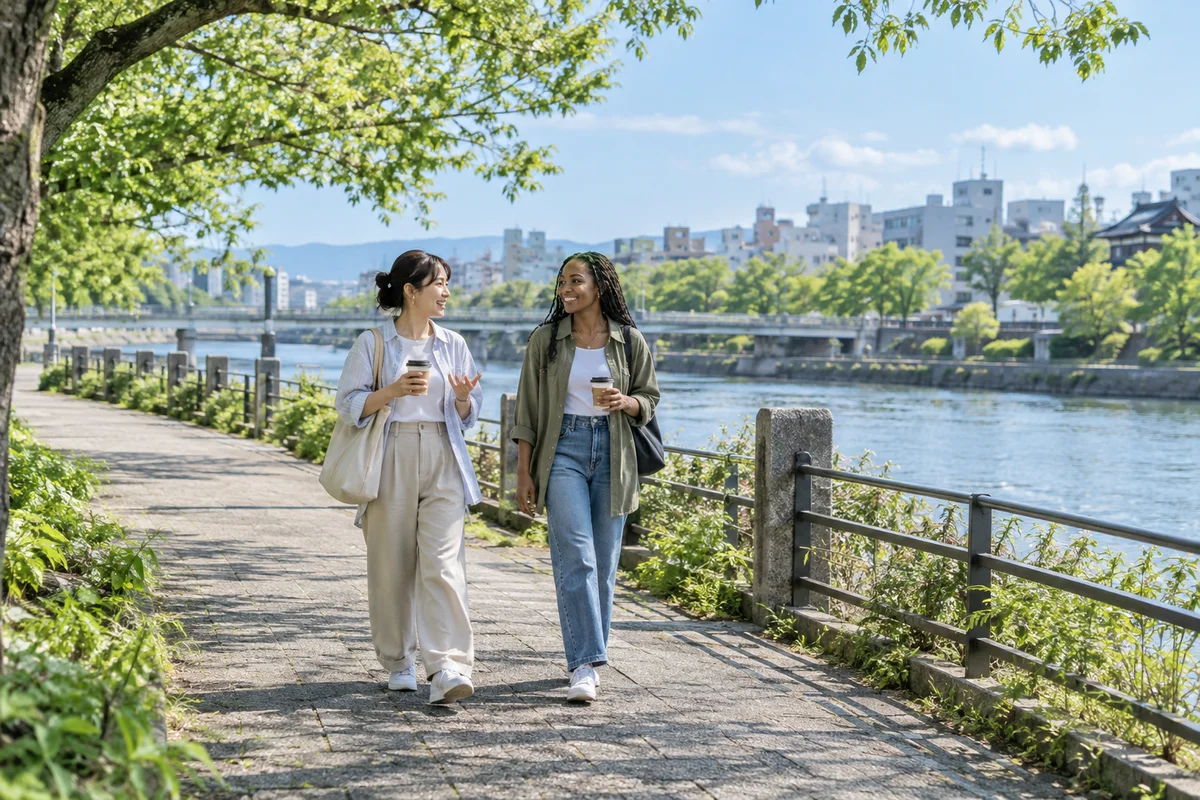 Two adult friends chatting on a sunny riverside walk in Japan